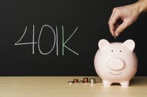 401(k) piggy bank with stacks of coins, and a hand pacing coin in the bank