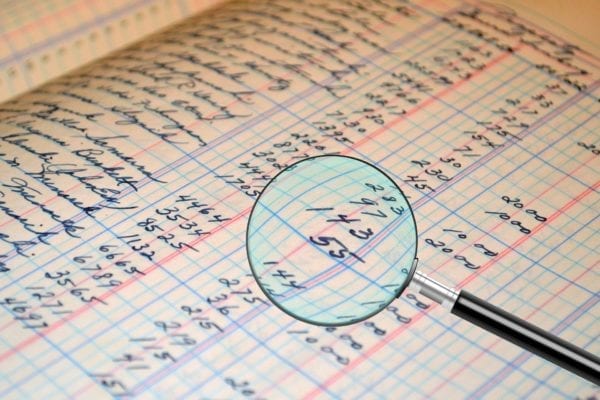 a magnifying glass inspecting a bookkeeping ledger for an audit